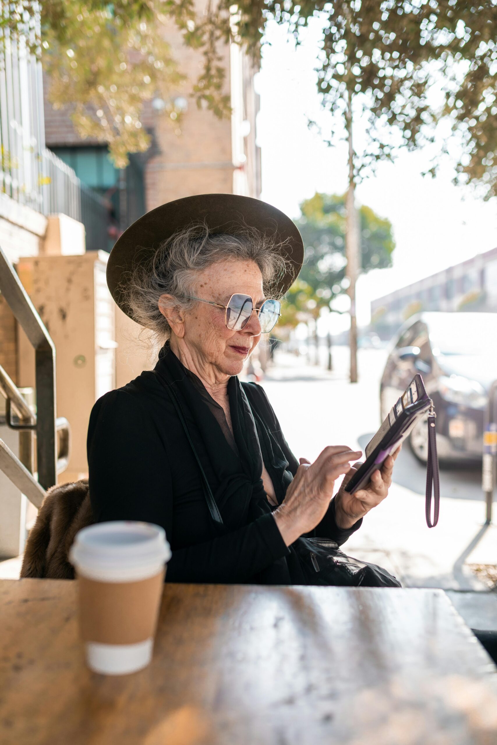 Stylish senior woman in sunglasses using tablet outdoors at a cafe.